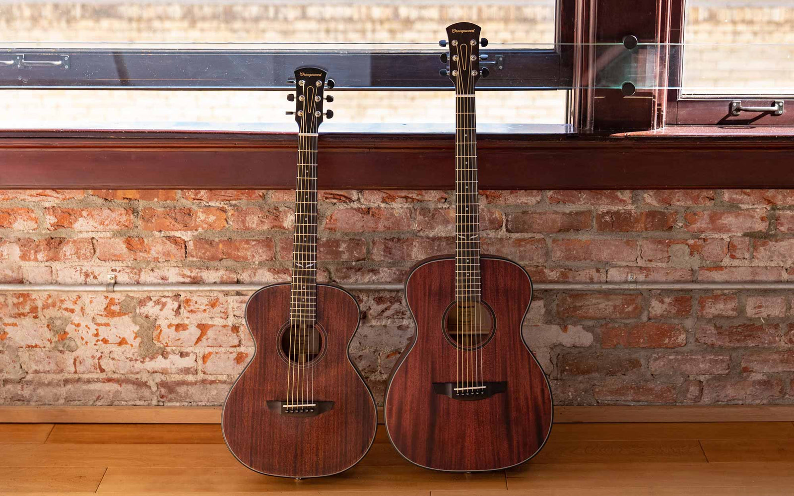 Oliver Jr. Mahogany and Oliver Mahogany guitars against a brick wall